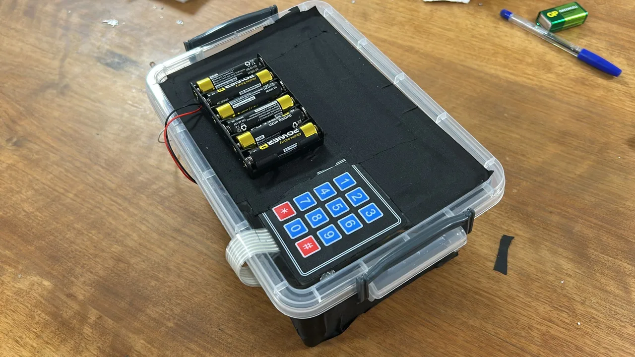 The assembled alarm in a plastic enclosure, with a numeric keypad and battery pack on its lid.